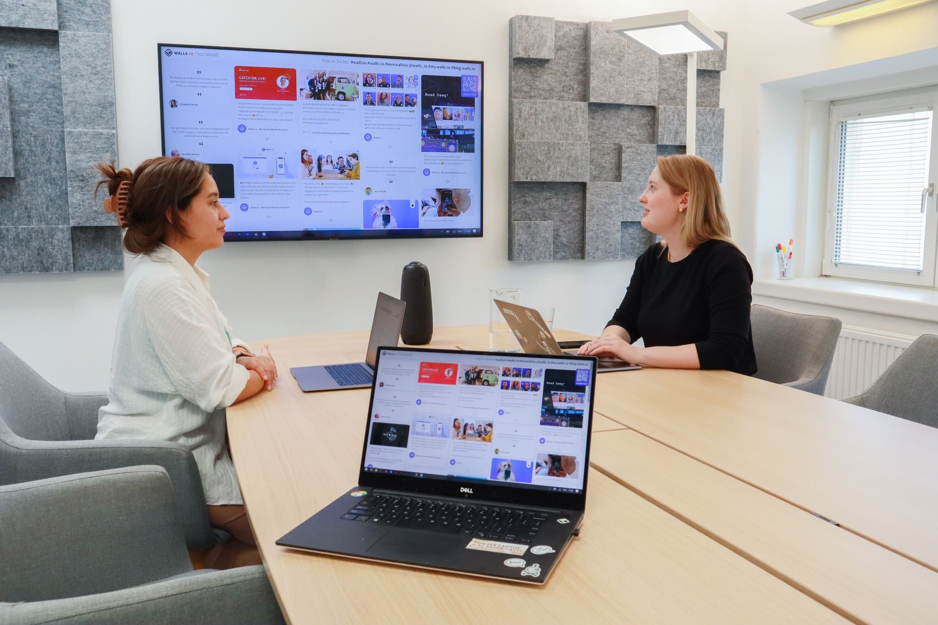 Women collaborating in a modern office with laptops and a large digital display